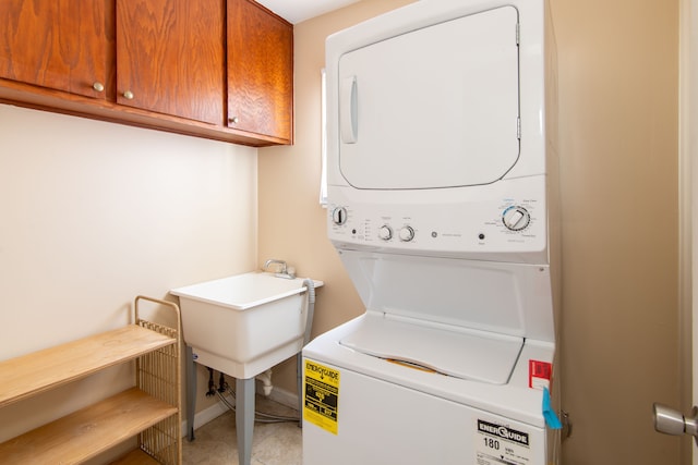 clothes washing area featuring stacked washer / drying machine, cabinet space, baseboards, and light tile patterned floors