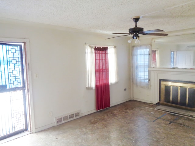 unfurnished living room with a glass covered fireplace, a ceiling fan, visible vents, and a textured ceiling