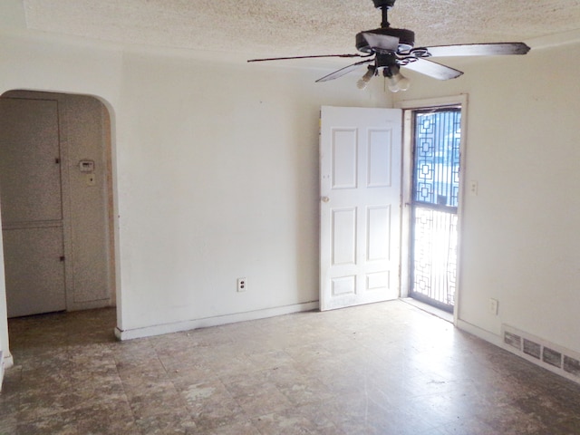 empty room featuring ceiling fan, a textured ceiling, baseboards, arched walkways, and visible vents