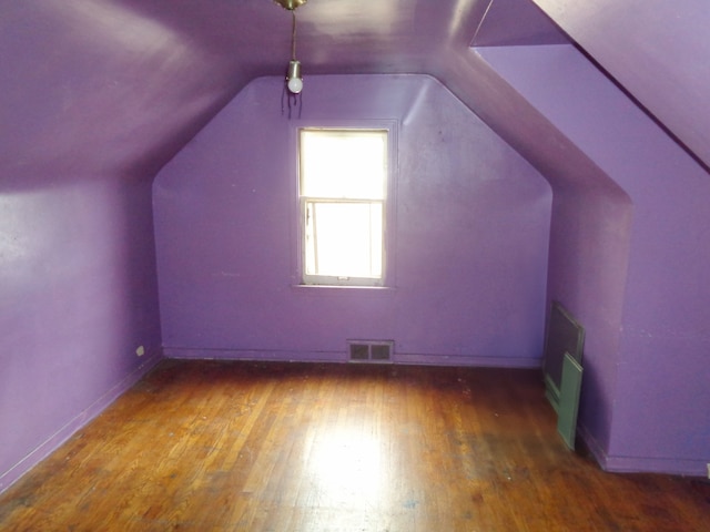 additional living space with wood finished floors, baseboards, vaulted ceiling, and visible vents