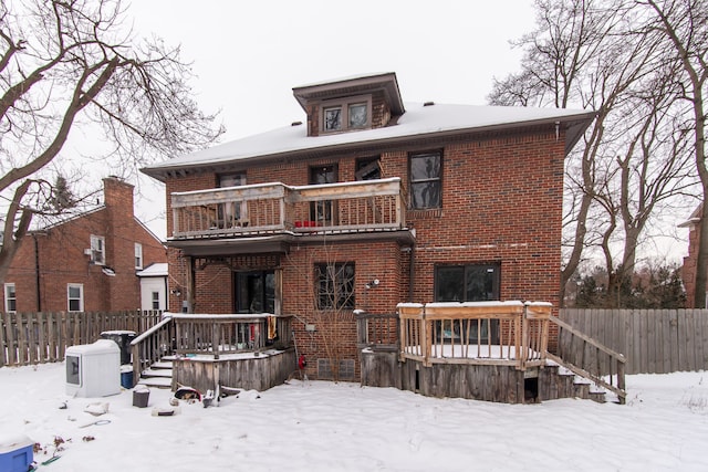 snow covered back of property with a balcony and a wooden deck