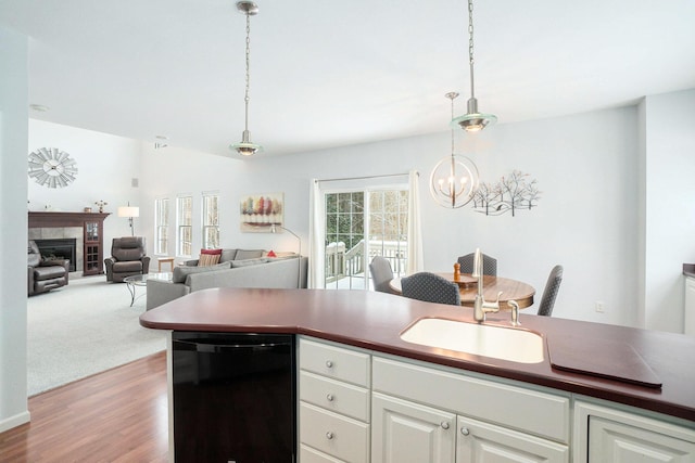 kitchen featuring sink, white cabinetry, black dishwasher, a tile fireplace, and pendant lighting