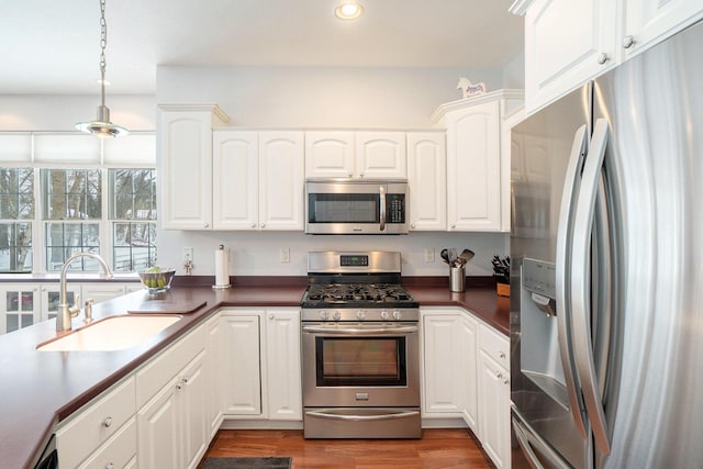 kitchen featuring pendant lighting, sink, appliances with stainless steel finishes, white cabinetry, and light wood-type flooring