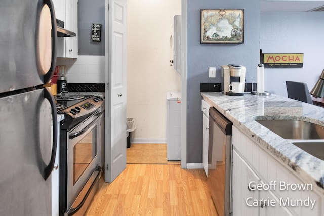 kitchen with white cabinetry, light stone counters, light hardwood / wood-style flooring, appliances with stainless steel finishes, and decorative backsplash