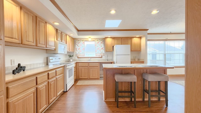 kitchen with light wood-type flooring, a breakfast bar, ornamental molding, light brown cabinets, and white appliances