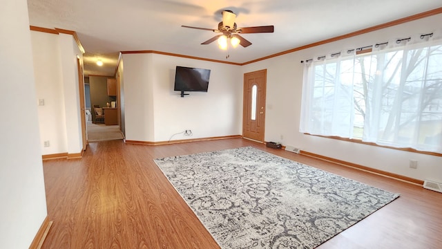 unfurnished living room featuring a ceiling fan, baseboards, visible vents, light wood-style floors, and crown molding