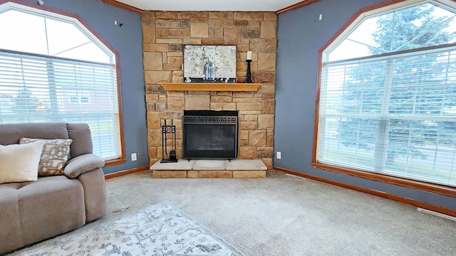 living area with a stone fireplace, crown molding, carpet, and baseboards