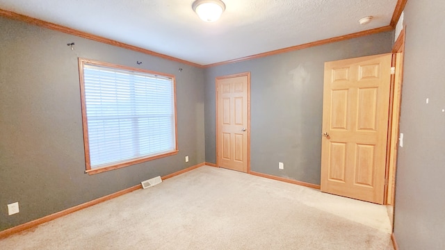 carpeted spare room featuring visible vents, a textured ceiling, crown molding, and baseboards