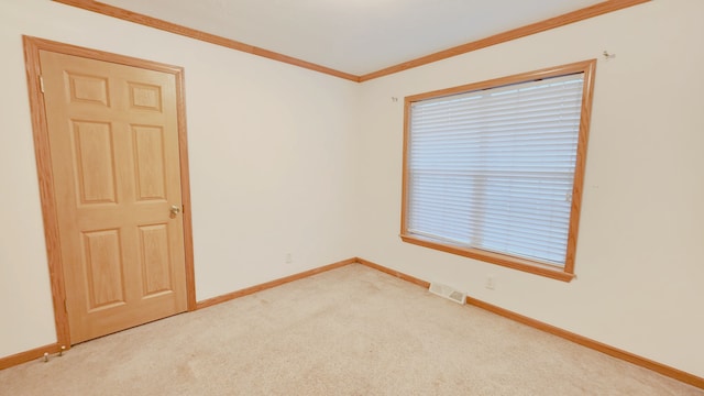 empty room with visible vents, light colored carpet, crown molding, and baseboards