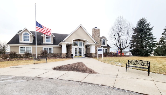 view of front facade with stone siding, french doors, concrete driveway, a front yard, and a chimney