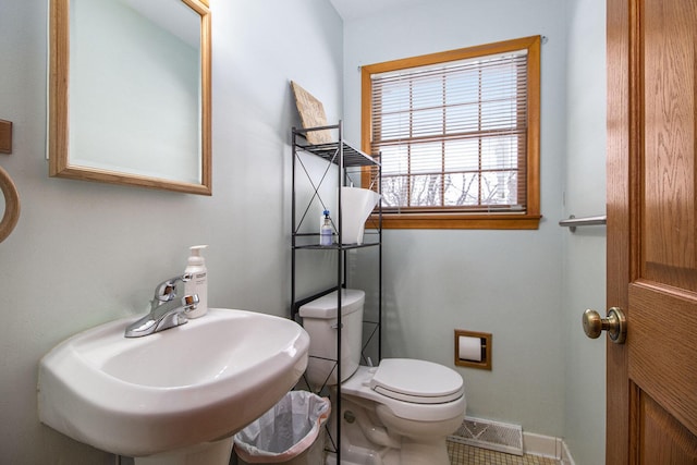 half bath with toilet, a sink, visible vents, and baseboards