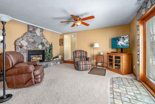 carpeted living room with a stone fireplace, a textured ceiling, and ceiling fan