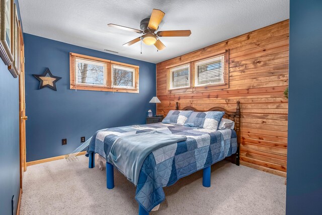 carpeted bedroom with a textured ceiling, wooden walls, and ceiling fan