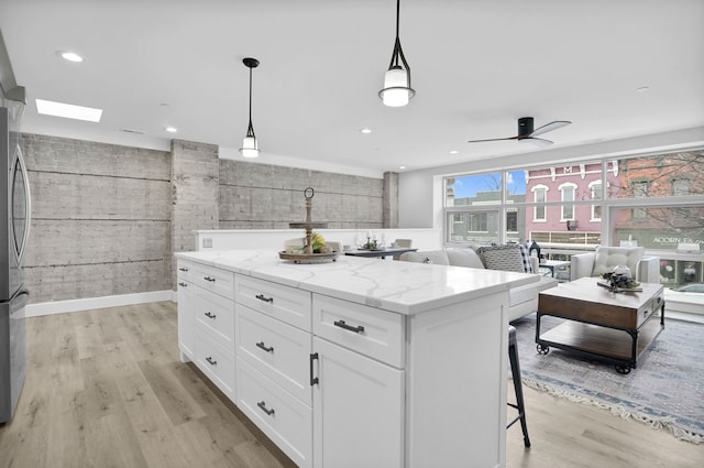 kitchen featuring light stone counters, a breakfast bar area, white cabinetry, a center island, and light wood finished floors