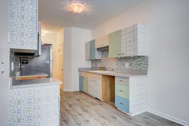 kitchen with sink, backsplash, stainless steel refrigerator, and light hardwood / wood-style flooring