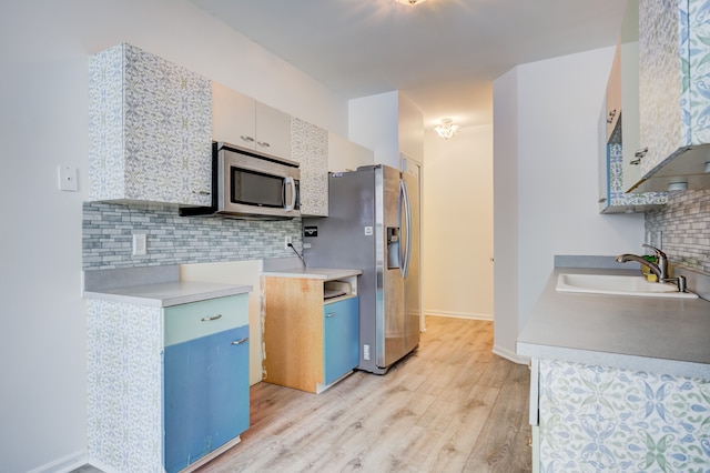 kitchen featuring sink, backsplash, appliances with stainless steel finishes, and light hardwood / wood-style flooring