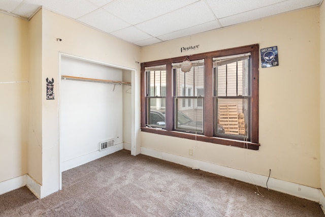 unfurnished bedroom with baseboards, visible vents, a drop ceiling, a closet, and carpet flooring