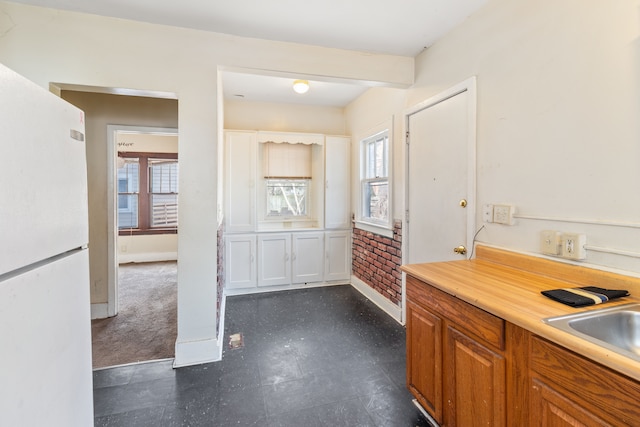 kitchen featuring baseboards, light countertops, brown cabinets, freestanding refrigerator, and a sink