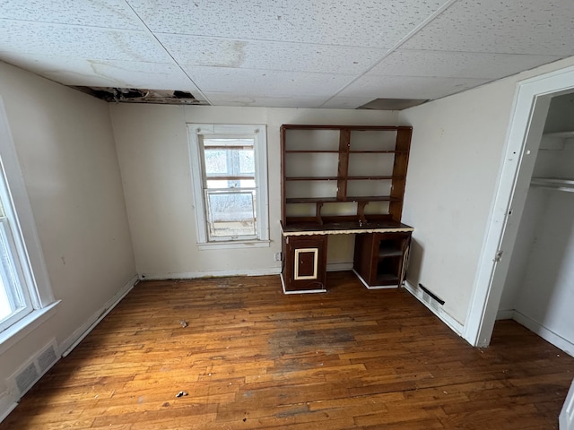 unfurnished office featuring a drop ceiling, visible vents, baseboards, dark wood-style floors, and built in desk