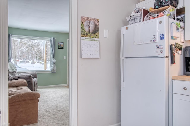 kitchen featuring light carpet, white fridge, and white cabinets