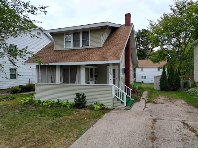 bungalow-style home featuring a front yard, a sunroom, roof with shingles, and a chimney