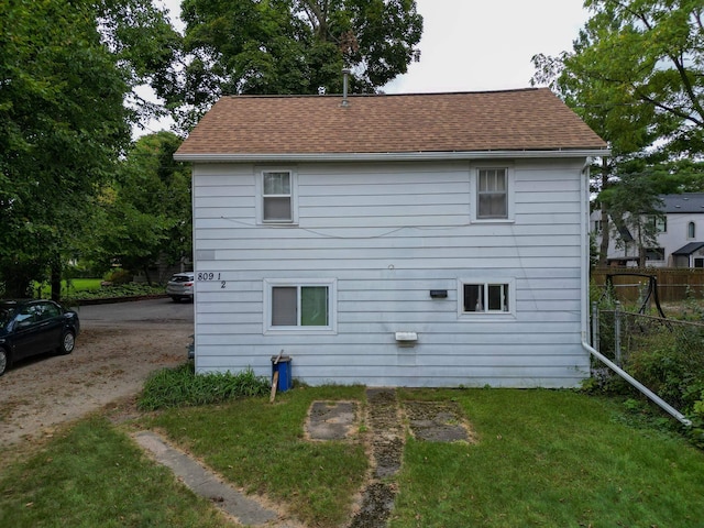 rear view of property with fence, a lawn, and roof with shingles