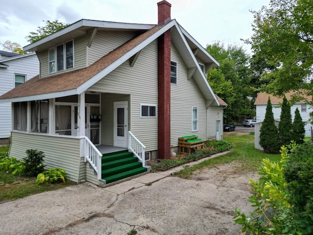 bungalow featuring a sunroom, roof with shingles, and a chimney