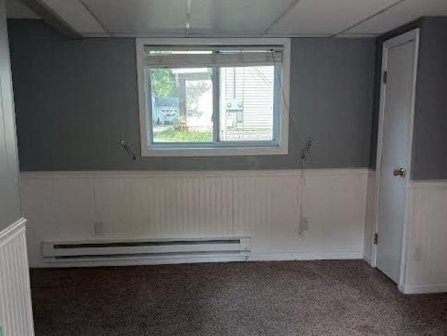 empty room with a drop ceiling, wainscoting, carpet flooring, and a baseboard radiator