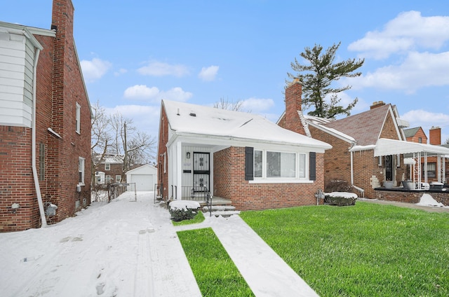 bungalow-style home featuring an outdoor structure, brick siding, a detached garage, and a front lawn