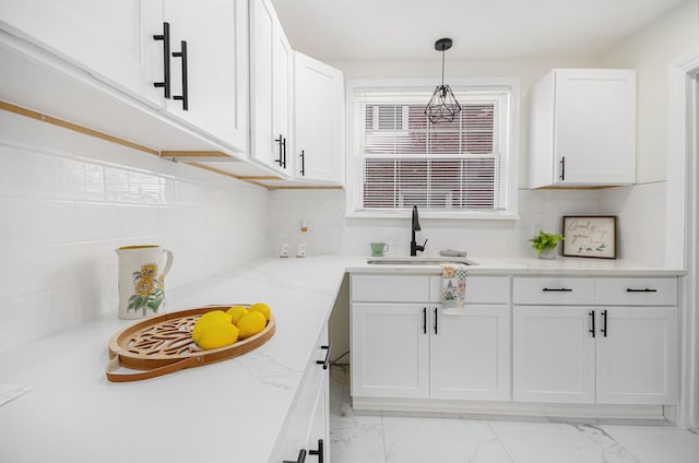 kitchen featuring marble finish floor, white cabinetry, a sink, and decorative light fixtures