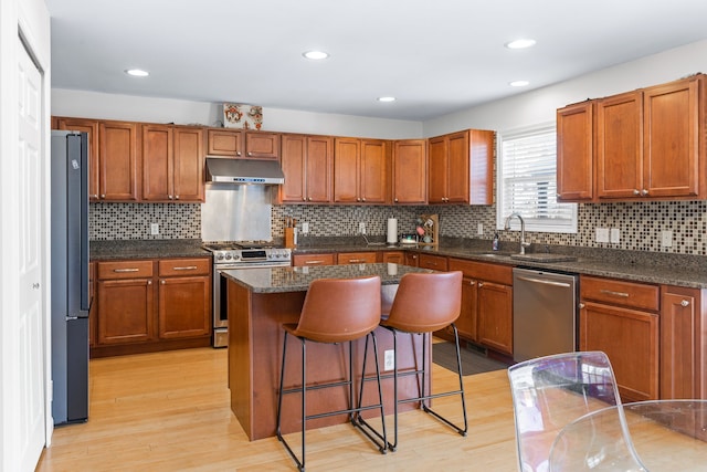 kitchen featuring appliances with stainless steel finishes, light hardwood / wood-style flooring, a kitchen island, sink, and a kitchen bar