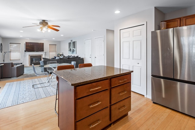 kitchen with dark stone counters, a kitchen island, light hardwood / wood-style floors, ceiling fan, and stainless steel fridge