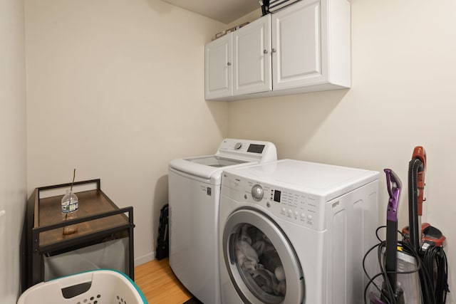 clothes washing area with washing machine and dryer, cabinets, and light wood-type flooring