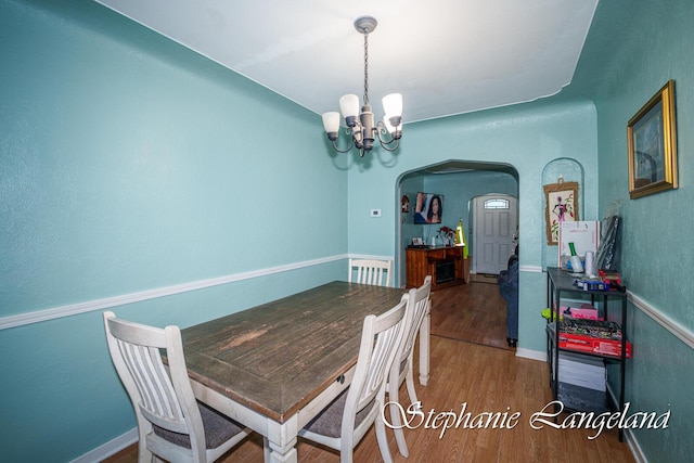 dining area with arched walkways, wood finished floors, a chandelier, and baseboards