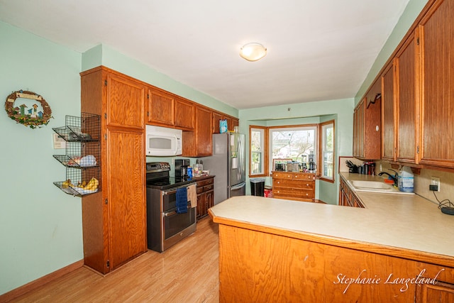 kitchen with light wood-type flooring, stainless steel appliances, a sink, and brown cabinets