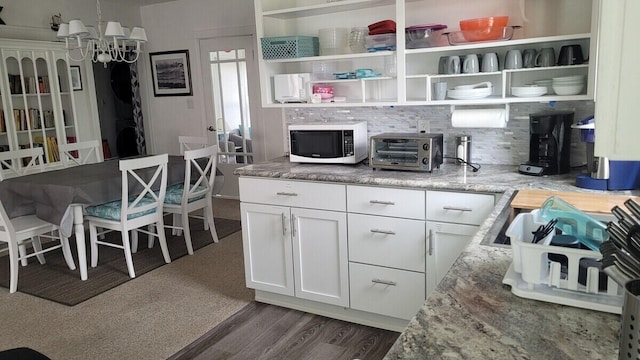 kitchen with white cabinetry, backsplash, dark hardwood / wood-style flooring, a chandelier, and light stone counters