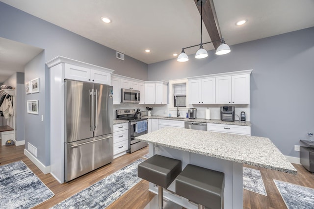 kitchen featuring sink, appliances with stainless steel finishes, a kitchen island, pendant lighting, and white cabinets