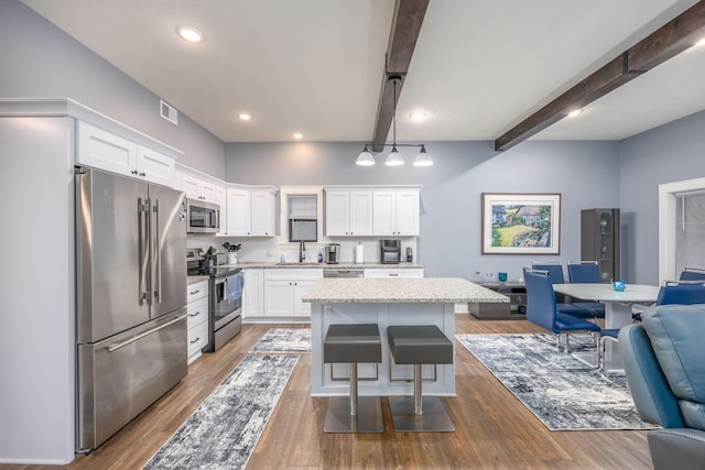 kitchen featuring a kitchen island, appliances with stainless steel finishes, a breakfast bar, white cabinetry, and beam ceiling