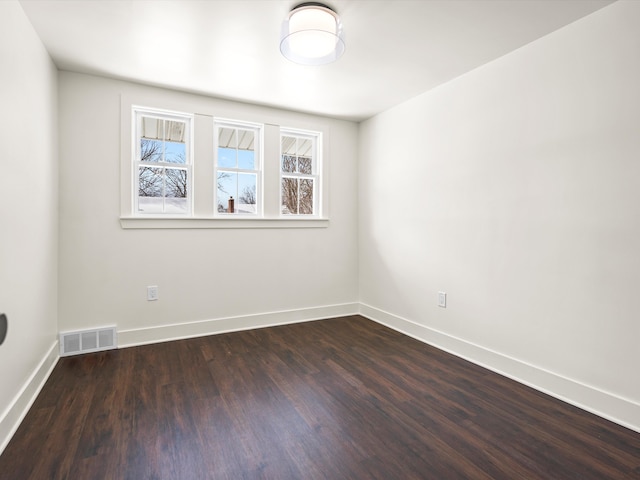 unfurnished room with dark wood-style floors, visible vents, and baseboards