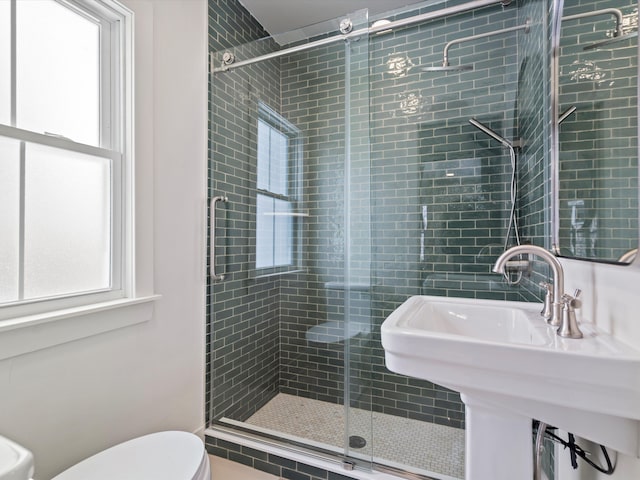 bathroom featuring toilet, a sink, a shower stall, and a wealth of natural light