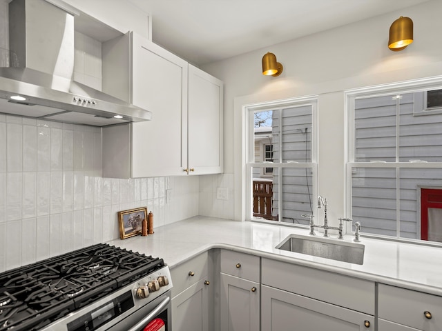 kitchen with tasteful backsplash, light countertops, stainless steel gas stove, a sink, and wall chimney range hood