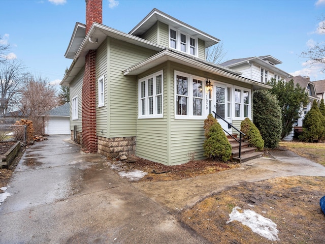 view of front of home with a garage, entry steps, an outdoor structure, and a chimney