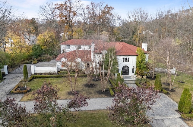 view of front facade featuring driveway, stucco siding, a chimney, a gate, and a front yard