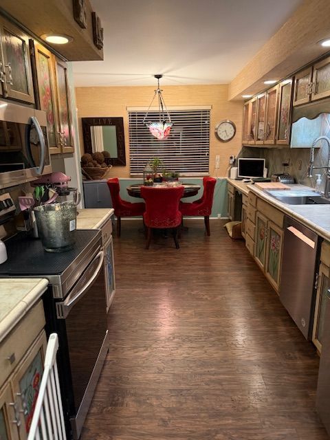 kitchen with dark wood-style flooring, light countertops, a sink, decorative light fixtures, and stainless steel appliances