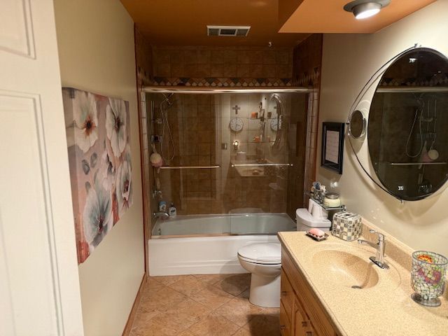 bathroom with visible vents, vanity, toilet, tile patterned floors, and enclosed tub / shower combo