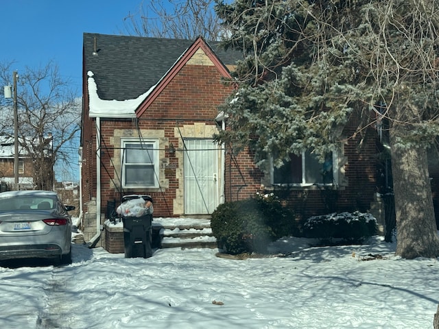 view of front of property featuring brick siding and roof with shingles