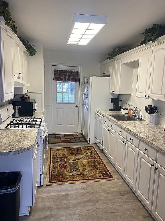 kitchen with sink, white appliances, light hardwood / wood-style flooring, and white cabinets