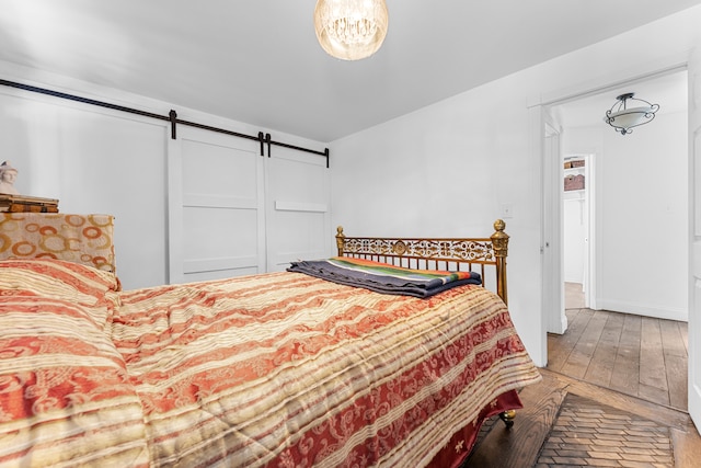 bedroom with a barn door, wood-type flooring, and baseboards