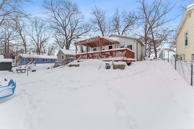 snow covered back of property with a garage, a pergola, and a wooden deck