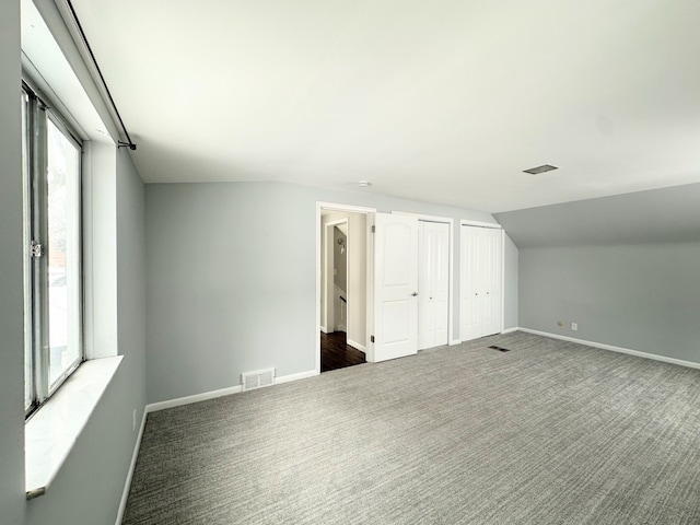 interior space featuring two closets, dark colored carpet, and vaulted ceiling